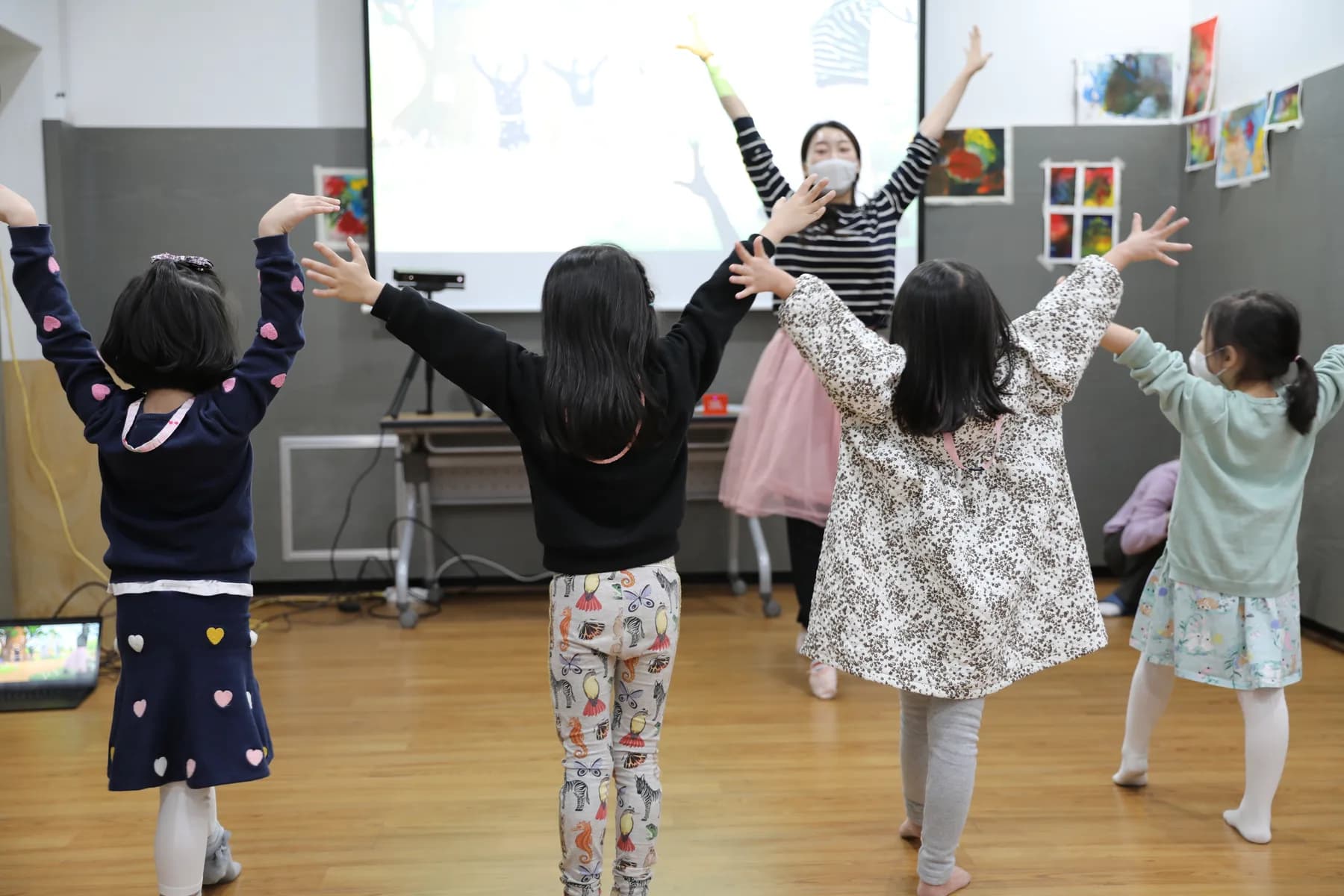 유치원 교실에서 아이들이 화면 속 TeachAble Art Play 영상을 보며 교사와 함께 두 팔을 벌리는 실제 수업 장면